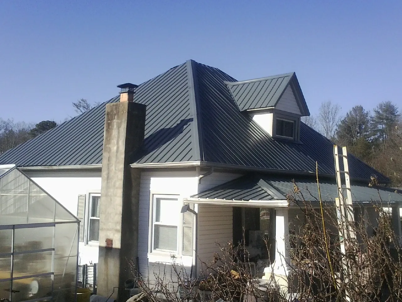 Dark blue standing seam metal roof on a white farmhouse with dormer — Slate & Tile Roof Repair by Roofing Brothers in Glyndon