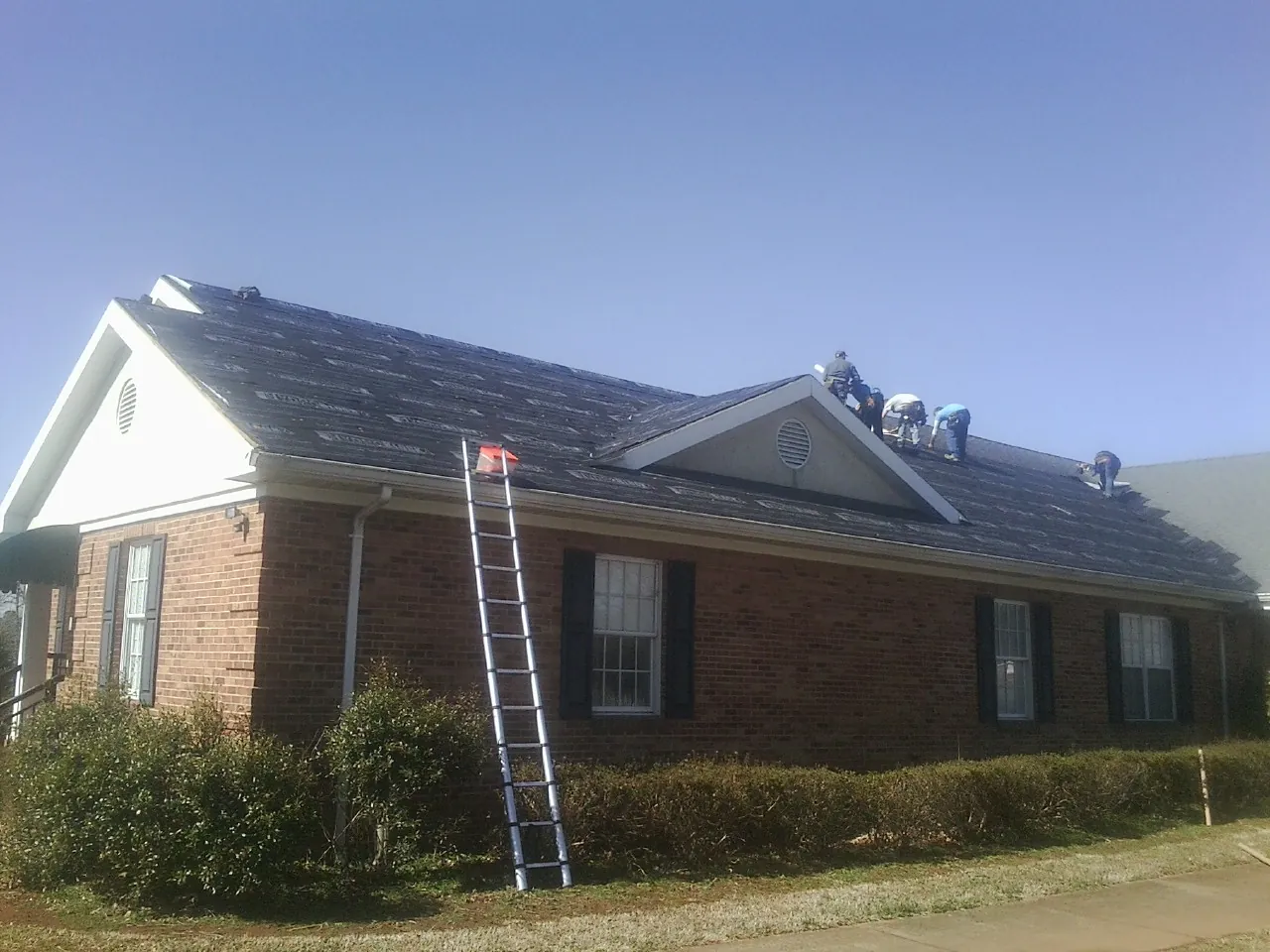 Crew tearing shingles off a brick ranch roof with a ladder set — Emergency Roof Repair work by our crew in Glyndon