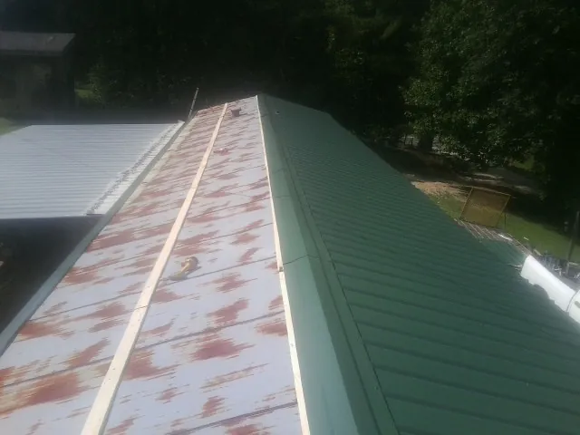 Old rusted panels beside newly installed green metal roofing — Wind Damage Roof Repair by Roofing Brothers in Glyndon