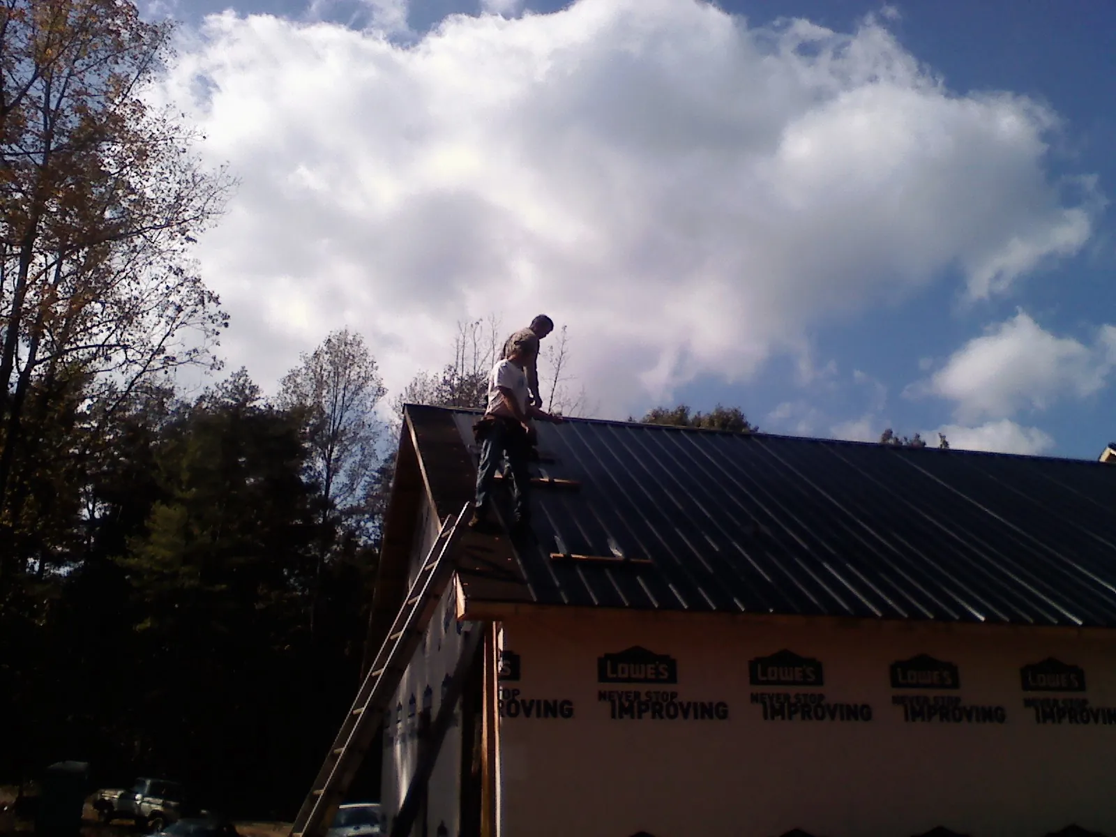 Roofer fastening dark metal panels high against a cloudy sky, from a Roof Inspection job in Glyndon